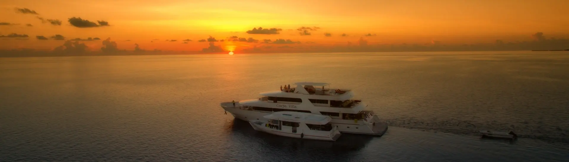 Carpe Vita liveaboard & dhoni in the Maldives, with the sun setting behind it
