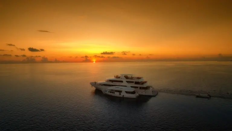 Carpe Vita liveaboard & dhoni in the Maldives, with the sun setting behind it